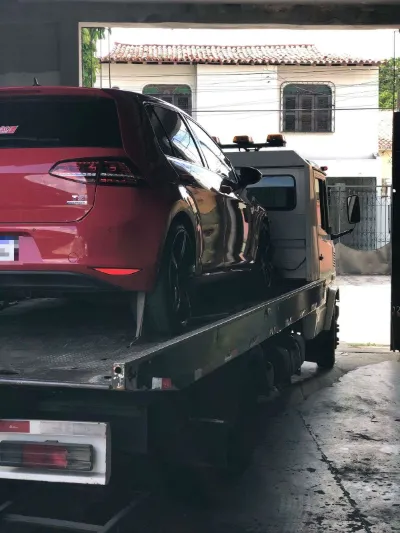 Hatch vermelho sobre a plataforma do guincho saindo de uma garagem