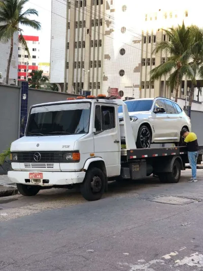 SUV branco sendo preso na plataforma do guincho em frente a prédios com coqueiros